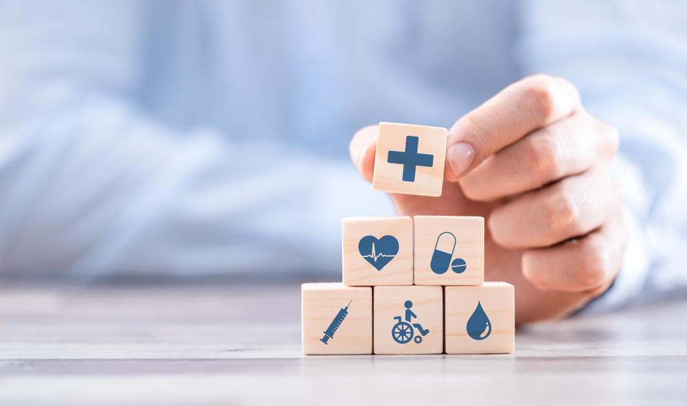 Hand arranging wood block with healthcare medical icon meant to signify the building blocks of regulatory change management in healthcare