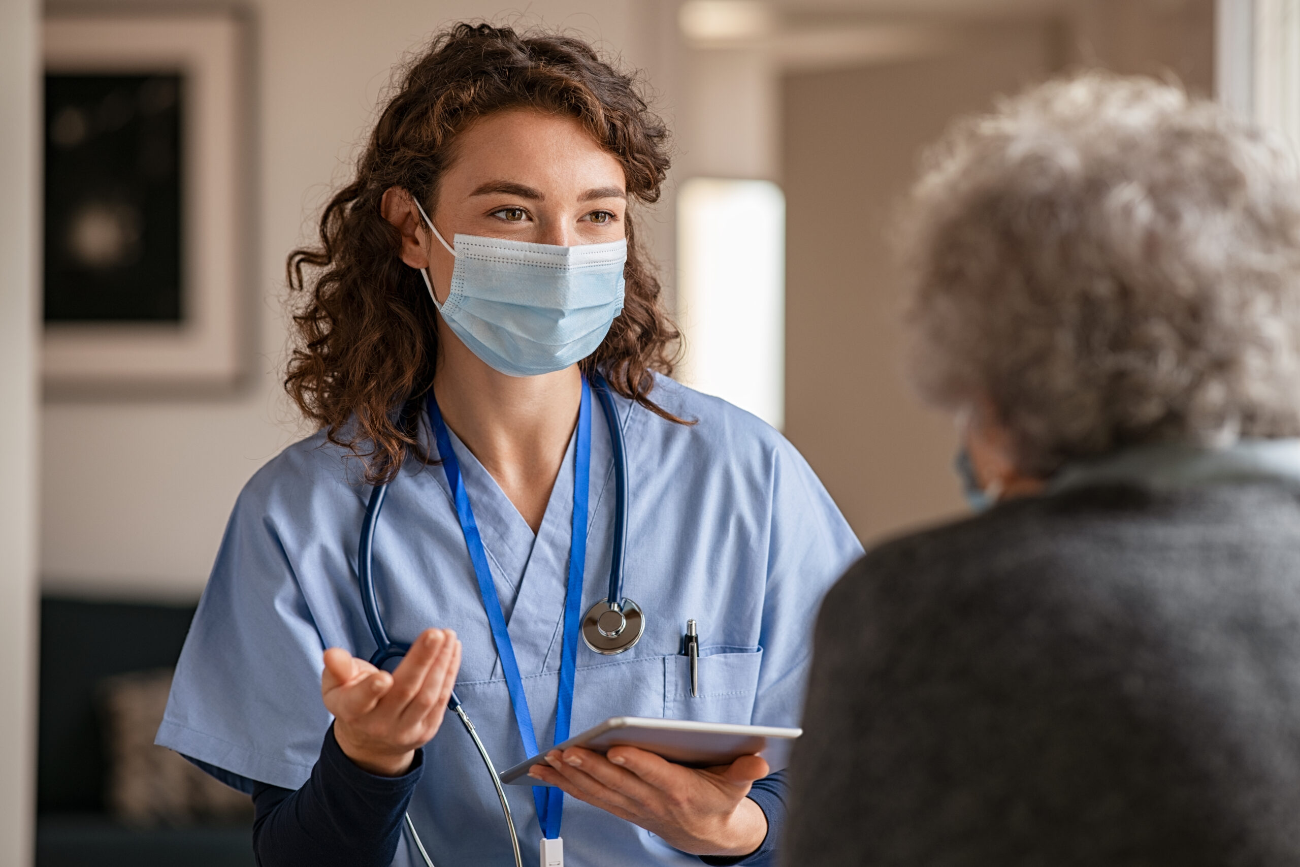 a masked doctor with long curly hair speaking with a elderly patient